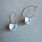 A pair of porcelain earrings with a semi-circular shape and steel underglaze, attached to gold-filled hoops, displayed against a grey background.
